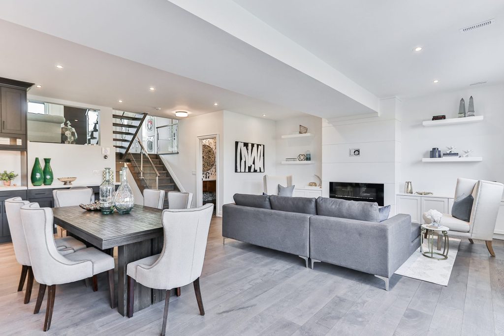 Home remodeling open-concept living and dining room with modern gray and white decor, featuring a large gray sectional, elegant dining table, and minimalist shelving.