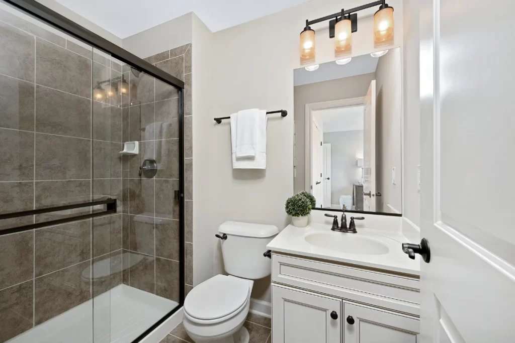 Modern bathroom remodeling with glass-enclosed shower, classic white vanity, black fixtures, and industrial-style lighting - ideal small bathroom design.