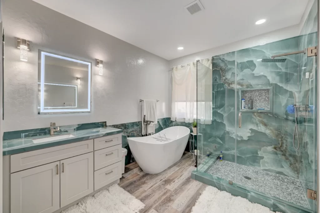 Modern bathroom renovation featuring a freestanding bathtub, glass-enclosed shower with green marble-style tiles, white vanity with LED mirror, and wood-look flooring at 7012 W Haldir Ave12.